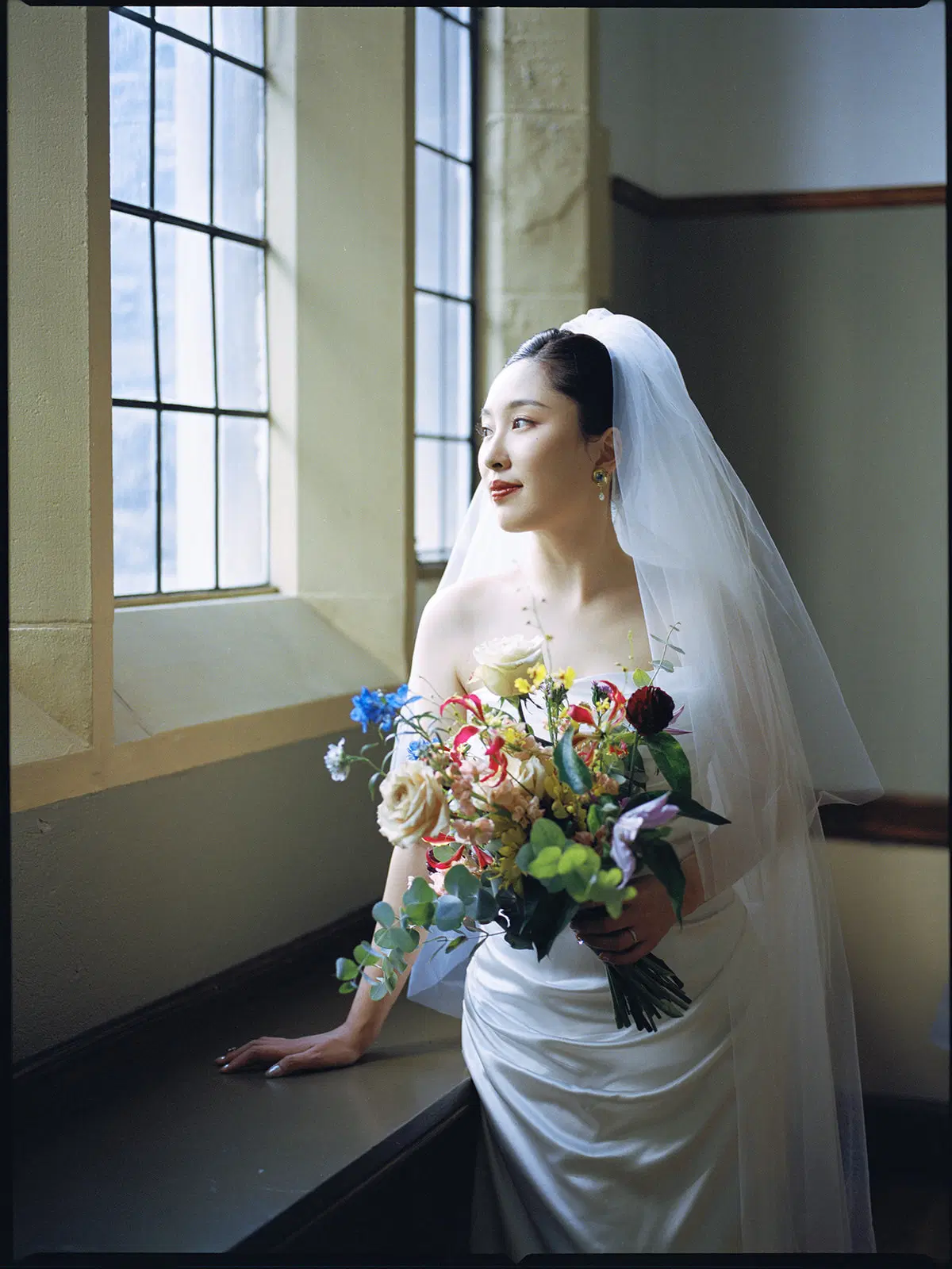Bridal portrait by a window with a colorful bouquet
