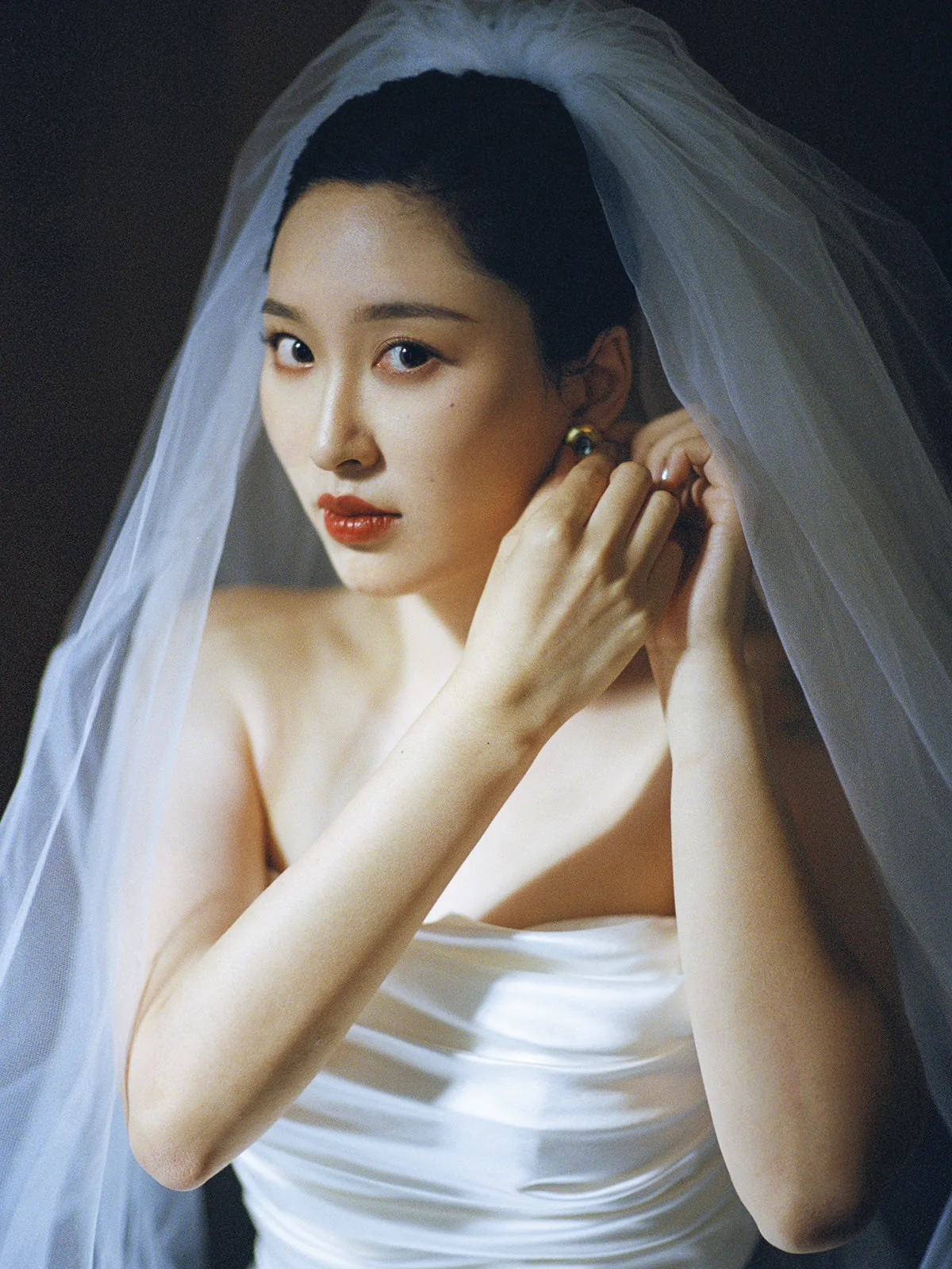 Bride adjusting an earring beneath her veil